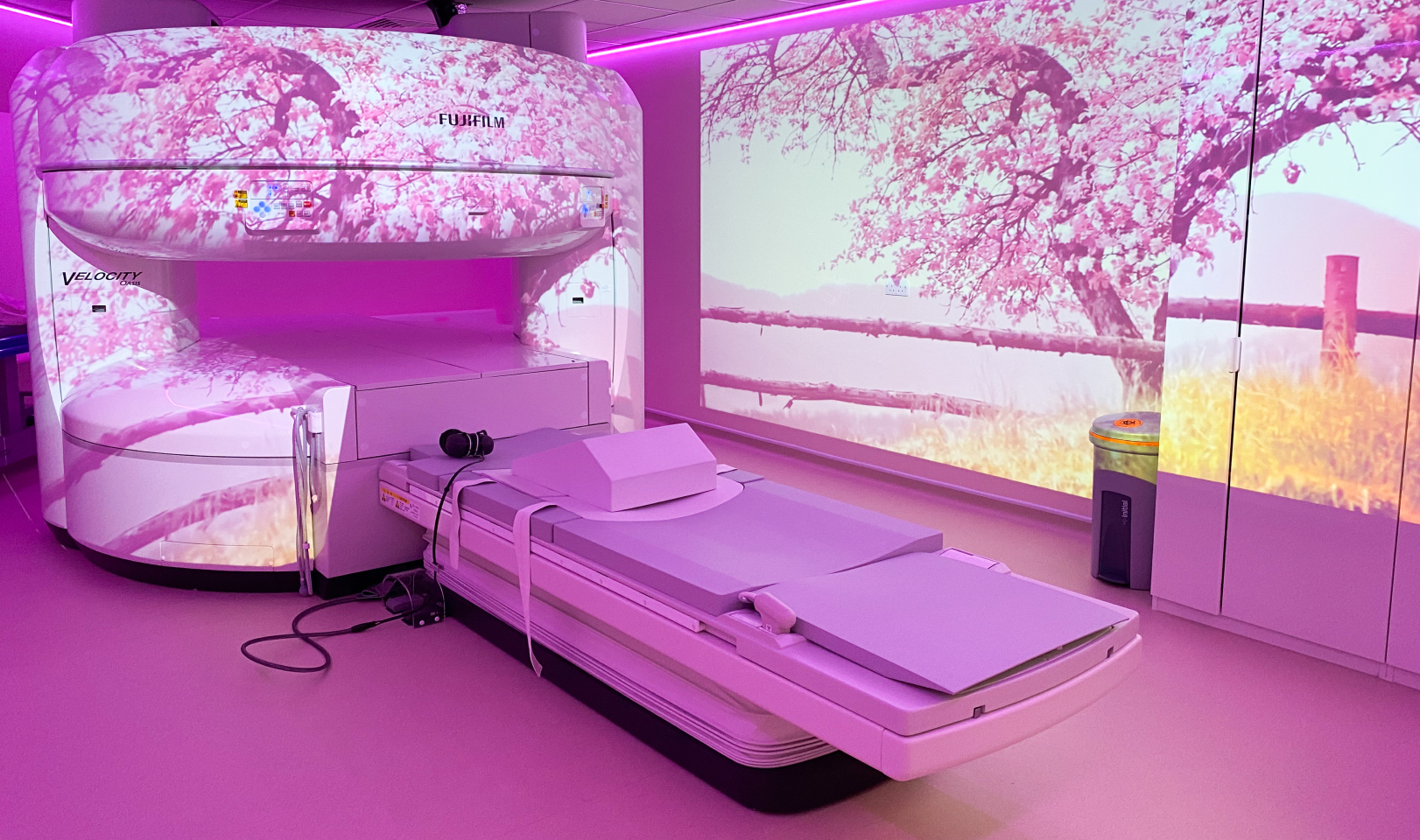 The open MRI scanner in the room features a projector, ensuring patients are entertained during their scans. The spacious design is particularly welcoming for children, making their experience more comfortable and less intimidating. This innovative setup creates a calming and engaging environment for all patients.